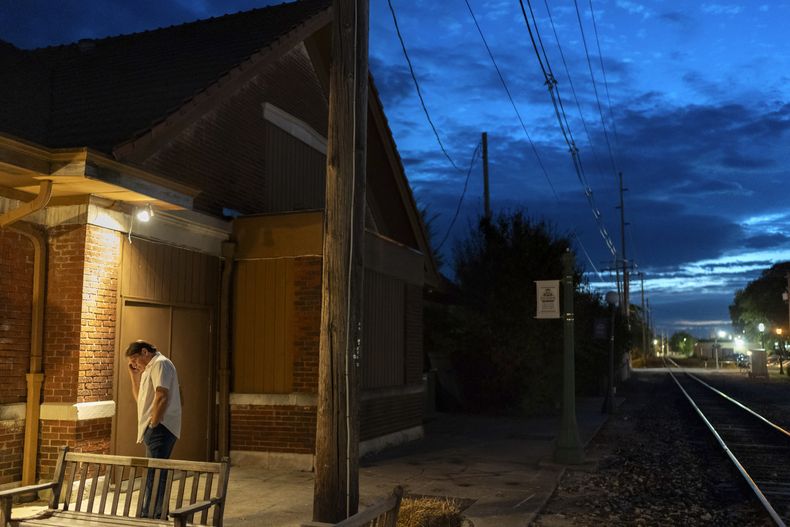 Matt Dzik habla con su hijo por teléfono en el exterior del teatro The Station mientras trabaja como acomodador voluntario durante una representación el sábado 21 de septiembre de 2024, en Urbana, Illinois. Matt y su esposa, Lesley, que disfrutan yendo a conciertos y espectáculos, trabajan juntos como voluntarios en el teatro local para poder ver las funciones gratis. (AP Foto/David Goldman)