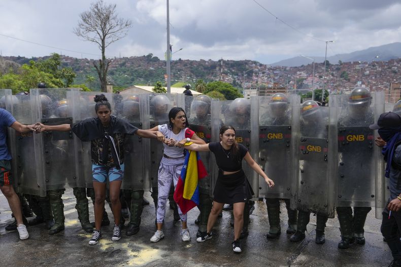 Varios ciudadanos intentan bloquear una calle en protesta por los resultados oficiales el día después de las elecciones presidenciales mientras agentes de la Guardia Nacional crean una línea de contención detrás de ellos en Caracas, Venezuela, el lunes 29 de julio de 2024. (AP Foto/Cristian Hernández)