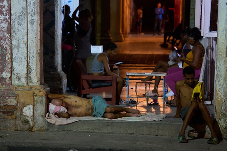 Un hombre duerme en la puerta de su casa mientras otros pasan el tiempo tratando de refrescarse en la calle en La Habana, Cuba, el martes 4 de agosto de 2026. (AP Foto/Ramón Espinosa)