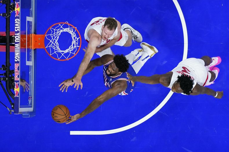 Joel Embiid, de los 76ers de Filadelfia, salta para encestar ante Jakob Poeltl (arriba) y O.G. Anunoby, de los Raptors de Toronto, el jueves 2 de noviembre de 2023 (AP Foto/Matt Slocum)