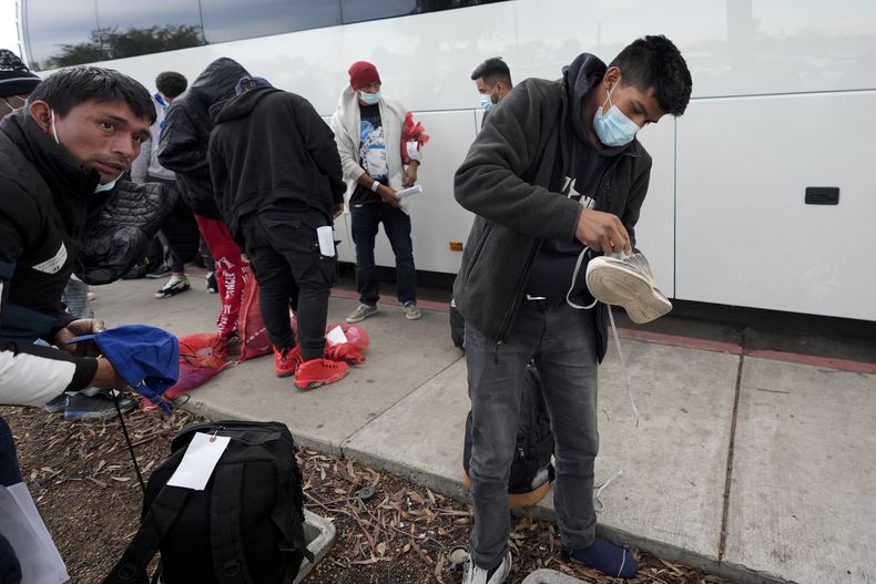 Migrantes descargan sus cosas de un autobús a su llegada a una parada de autobuses tras salir de una instalación de procesamento, el viernes 23 de febrero de 2024, en San Diego. (AP Foto/Gregory Bull)