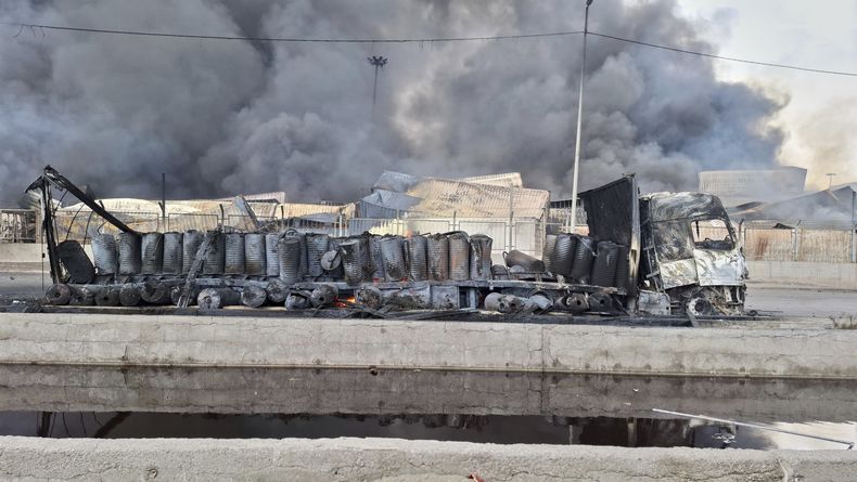 El humo se eleva en el fondo junto a los restos destrozados de un camión, el domingo 27 de abril de 2025, después de una enorme explosión en un puerto cerca de la ciudad portuaria sureña de Bandar Abbas, Irán, el sábado. (AP Foto/Meysam Mirzadeh/Tasnim News)