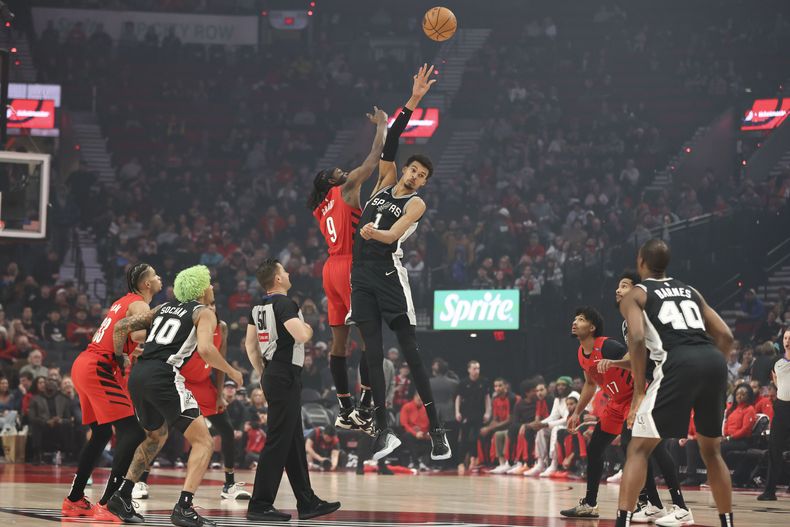 El jugador de los Trail Blazers de Portland Jerami Grant (9) y el de los Spurs de San Antonio Victor Wembanyama (1) saltan por el balón al inicio del partido de la NBA que enfrentó a ambos equipos el 13 de diciembre de 2024, en Portland, Oregon. (AP Foto/Amanda Loman)
