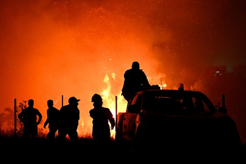 Las siluetas de bomberos y otras personas pueden captarse en medio de un incendio forestal el sábado 4 de julio de 2026, en las afueras de la ciudad de Salónica, en el norte de Grecia. (AP Foto/Giannis Papanikos)
