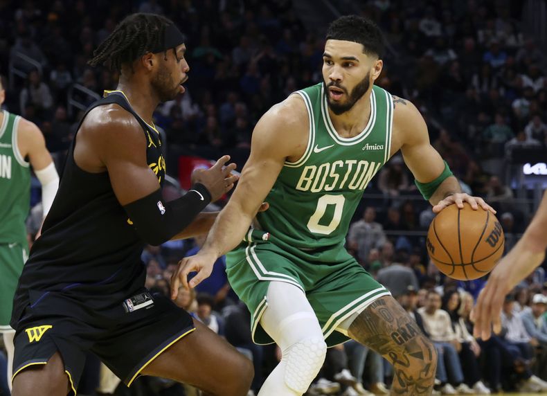 El alero de los Celtics de Boston, Jayson Tatum (0), conduce hacia la canasta contra el escolta de los Warriors de Golden State, Buddy Hield, a la izquierda, durante la primera mitad de un partido de baloncesto de la NBA en San Francisco, el lunes 20 de enero de 2025. (AP Foto/Jed Jacobsohn)