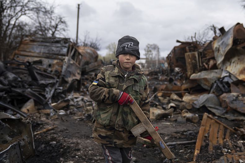 Yehor, de 7 años, sostiene un rifle de juguete junto a vehículos militares rusos destruidos cerca de Cherníhiv, Ucrania, el domingo 17 de abril de 2022. (AP Foto/Evgeniy Maloletka)