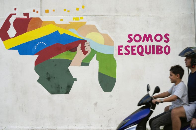 ARCHIVO – Un joven conduce una motocicleta frente a un mural que representa el mapa de Venezuela con el territorio de Esequibo, una franja de tierra administrada y controlada por Guyana, pero reclamada por Venezuela, en el barrio 23 de Enero en Caracas, Venezuela, 11 de diciembre de 2023. (AP Foto/Matias Delacroix, Archivo)