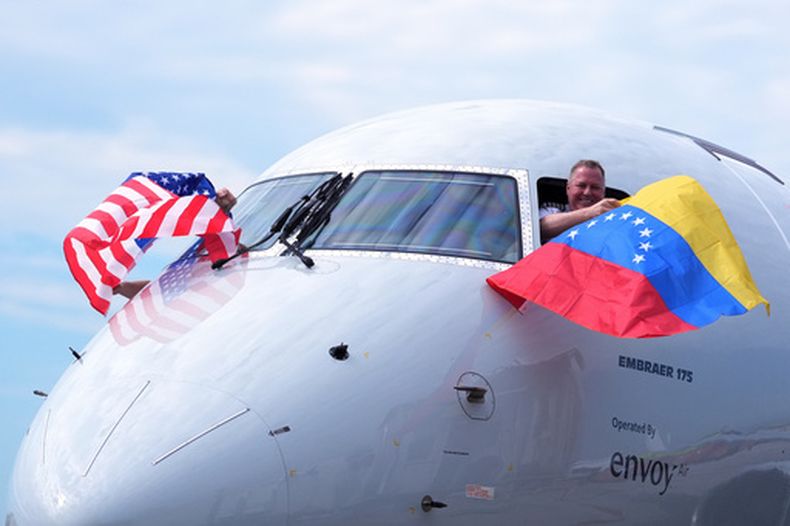 El capitán Ric Wilson ondea una bandera venezolana y el primer oficial saluda a la bandera estadounidense mientras se preparan para volar en el vuelo AA3599 de American Airlines, el primer vuelo comercial directo entre Estados Unidos y Venezuela en siete años, el jueves 30 de abril de 2026, en el Aeropuerto Internacional de Miami. (AP Foto/Rebecca Blackwell)