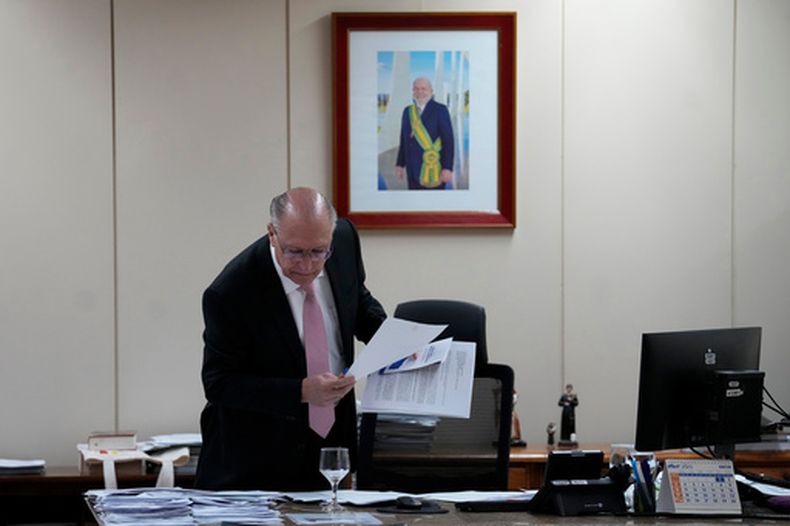 El vicepresidente de Brasil, Geraldo Alckmin, toma algunos papeles de un escritorio frente a una foto del presidente del país, Luiz Inácio Lula da Silva, antes de una entrevista en su oficina, en Brasilia, Brasil, el 22 de abril de 2026. (AP Foto/Eraldo Peres)