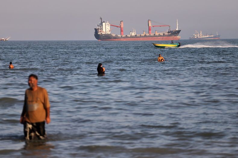Varios residentes nadan en las aguas del estrecho de Ormuz mientras un pequeño bote de motor pasa frente a buques de carga cerca de Bandar Abbas, Irán, el miércoles 17 de junio de 2026. (Amirhosein Khorgooi/ISNA vía AP)
