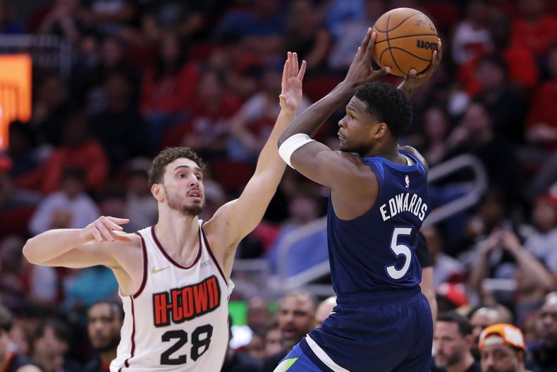 Anthony Edwards (5), de los Timberwolves de Minnesota, busca pasar el balón ante la presión defensiva de Alperen Sengun (28), de los Rockets de Houston, durante la primra mitad del juego de baloncesto de la NBA, el viernes 27 de diciembre de 2024, en Houston. (AP Foto/Michael Wyke)