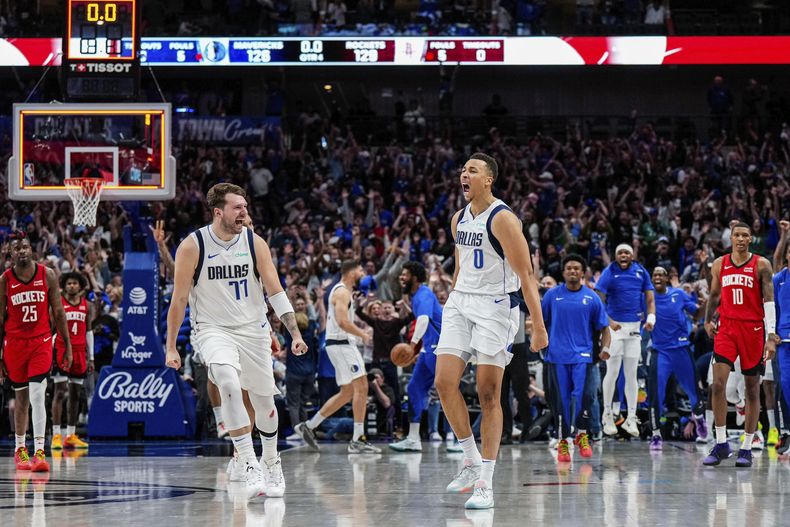 En esta foto proporcionada por los Mavericks de Dallas, Dante Exum (0) celebrating su triple de último segundo con su compañero Luka Doncic (77), mientras la afición en la arena celebra y los jugadores de los Rockets de Houston Reggie Bullock Jr. (25), Jabari Smith Jr. (10) y Jalen Green (4) observan al final del cuarto periodo del juego de baloncesto de la NBA, el domingo 7 de abril de 2024, en Dallas. (Dallas Mavericks vía AP)