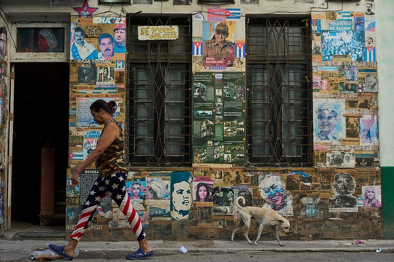 Una mujer que lleva unos pantalones con motivos de la bandera estadounidense pasa junto a un edificio que alberga una instalación artística sobre la Revolución Cubana, en la que se exhiben fotografías del expresidente cubano Raúl Castro y del expresidente venezolano Nicolás Maduro, en La Habana, Cuba, el martes 19 de mayo de 2026. (AP Foto/Ramón Espinosa)