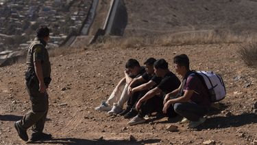 Un agente de la Patrulla Fronteriza pasa junto a cuatro hombres detenidos después de cruzar ilegalmente la frontera México-EEUU, el jueves 23 de enero de 2025, en San Diego. (AP Foto/Gregory Bull)