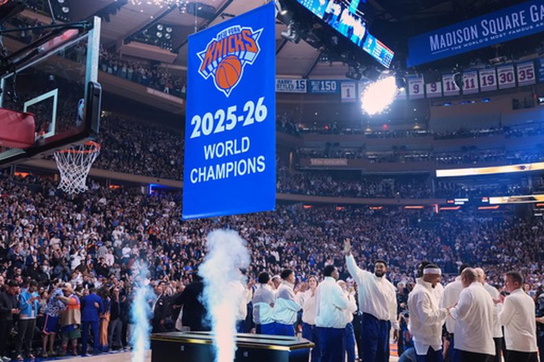 El pívot de los Knicks de Nueva York, Karl-Anthony Towns, saluda mientras se iza el estandarte de Campeones del Mundo 2025-26 de los Knicks antes de un partido de básquetbol de la NBA entre los Knicks y los 76ers de Filadelfia, el martes 20 de octubre de 2026, en Nueva York. (Foto AP/Frank Franklin II)
