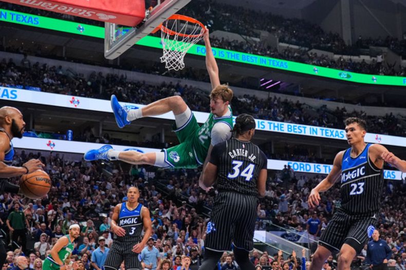 Cooper Flagg (32), de los Mavericks de Dallas, se cuelga del aro después de clavar el balón entre Wendell Carter Jr. (34) y Tristan da Silva (23) mientras Desmond Bane (3), del Magic de Orlando, observa en la primera mitad del juego de baloncesto de la NBA, el viernes 3 de abril de 2026, en Dallas. (AP Foto/Tony Gutierrez)