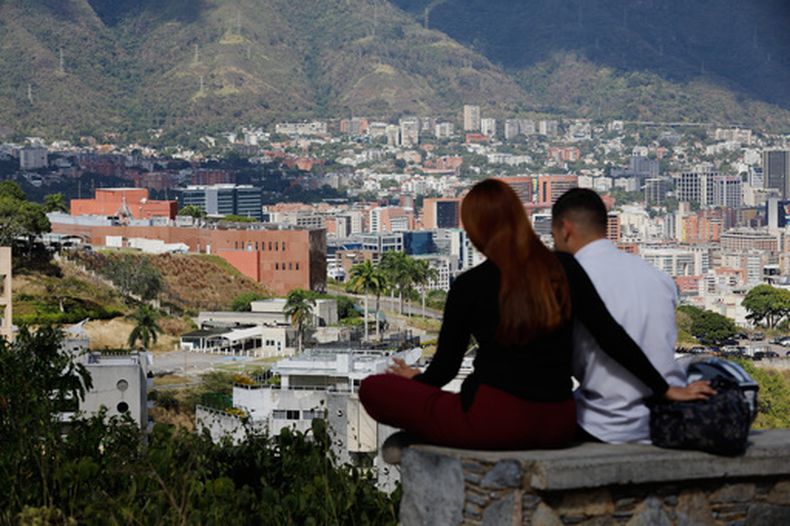 Una pareja sentada en un banco en un mirador con vistas a la embajada de Estados Unidos, en el centro a la izquierda, en Caracas, Venezuela, el viernes 9 de enero de 2026. (AP Foto/Cristian Hernández)
