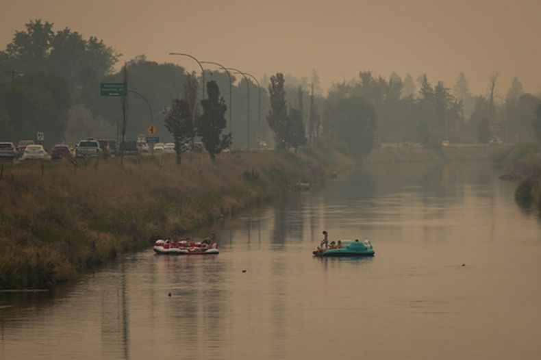 Personas se divierten en flotantes en el canal Pathway que conecta a los lagos Okanagan y Skaha en medio del humo provocado por los incendios forestales que arden en la región, el lunes 10 de agosto de 2026, en Penticton, Columbia Británica, Canadá. (Darryl Dyck/The Canadian Press via AP)