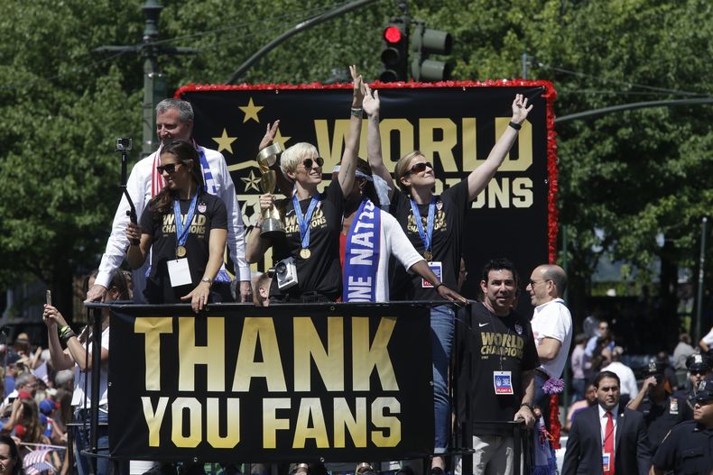 ARCHIVO - Foto del 10 de julio del 2015, la jugadora de la selección de Estados Unidos Megan Rapinoe saluda a los seguidores mientras sostiene el trofeo de campeón de la Copa Mundial durante el desfile acompañada del resto del equipo. (AP Foto/Mary Altaffer, Archivo)