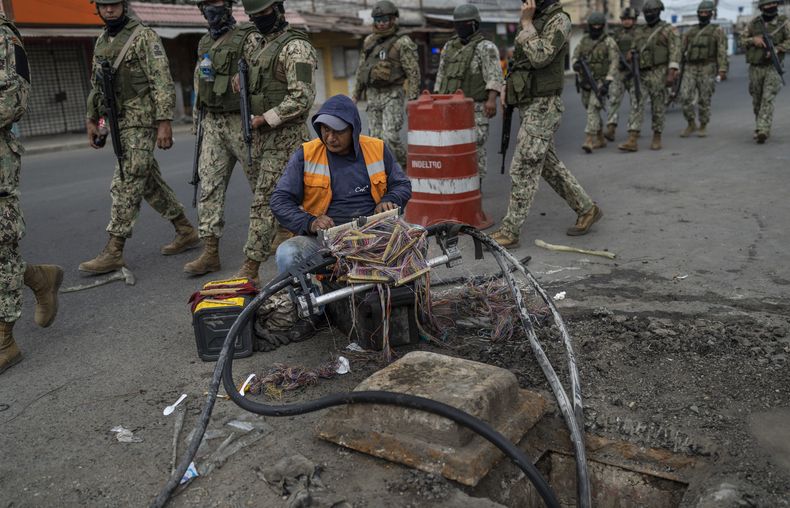 Un operario de una empresa de internet arregla el cableado mientras soldados patrullan por una calle de Durán, una ciudad ubicada frente a Guayaquil, Ecuador, el 30 de septiembre de 2023. (AP Foto/Rodrigo Abd)