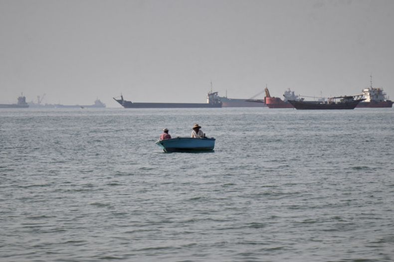 Dos hombres navegan en una pequeña embarcación mientras una serie de mercantes, petroleros y buques de servicios esperan en el horizonte, en el estrecho de Ormuz, frente a Bandar Abbas, Irán, el 27 de abril de 2026.(Razieh Poudat/ISNA vía AP)
