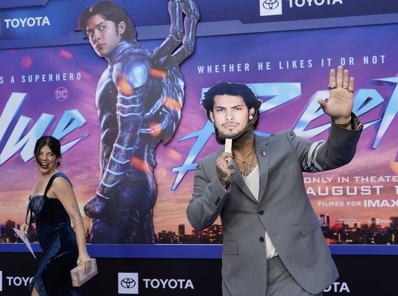 Angel Manuel Soto, derecha, director de Blue Beetle detrás de una máscara de Xolo Maridueña mientras lo ve su esposa Carla González, en una función de la película el 15 de agosto de 2023, en el Teatro Chino TCL en Los Angeles. Maridueña no pudo asistir a la premiere por la huelga de actores en Hollywood. (Foto AP/Chris Pizzello)