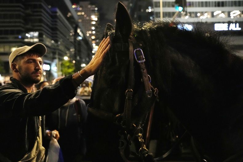 Un caballo policía es acariciado por un israelí que protesta contra los planes del gobierno ultraderechista del primer ministro Benjamin Netanyahu de reformar el sistema judicial en Tel Aviv, Israel, el sábado 29 de abril de 2023. (AP Foto/Ohad Zwigenberg)