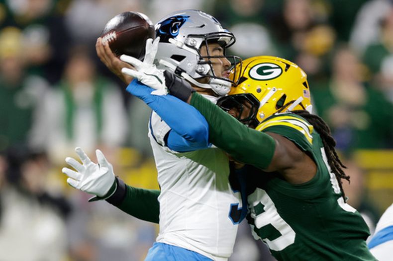 Bryce Young, izquierda, quarterback de los Panthers de Carolina, es golpeado por Tyron Hopper, derecha, linebacker de los Packers de Green Bay, mientras lanza un pase durante la primera mitad del partido de la NFL, el jueves 29 de octubre de 2026, en Green Bay, Wisconsin. (AP Foto/Matt Ludtke)