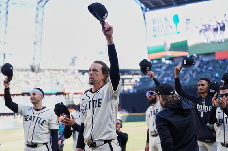 Los jugadores de los Marineros de Seattle, entre ellos el abridor Logan Gilbert, saludan al narrador de radio Rick Rizzs previo al último juego de su carrera ante los Angelinos de Los Ángeles, el domingo 27 de septiembre de 2026, en Seattle. (AP Foto/Lindsey Wasson)