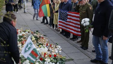 Personas con la bandera nacional estadounidense acuden a presentar sus condolencias a los tres soldados hallados muertos el lunes en un campo de entrenamiento de Pabrade, cerca de la embajada de Estados Unidos en Vilna, Lituania, martes 1 de abril de 2025. (AP foto/Mindaugas Kulbis)