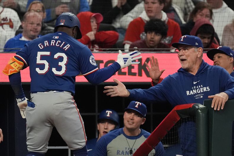 El cubano de los Rangers de Texas Adolis García (53) es felicitado por el mánager de los Rangers Bruce Bochy (derecha) en el banquillo luego de impactar un cuadrangular de dos carreras en la 8va entrada del juego ante los Bravos de Atlanta, el domingo 21 de abril de 2024, en Atlanta. (AP Foto/John Bazemore)