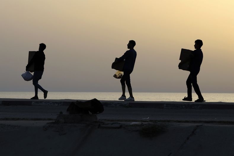 Palestinos cargan cajas con ayuda humanitaria luego de que camiones cargados de ésta llegaron a la Franja de Gaza desde un nuevo muelle flotante erigido por Estados Unidos, en un camino junto a la playa en el campamento de refugiados de Nusseirat, en el centro de la Franja de Gaza, el sábado 18 de mayo de 2024. (AP Foto/Saher Alghorra)