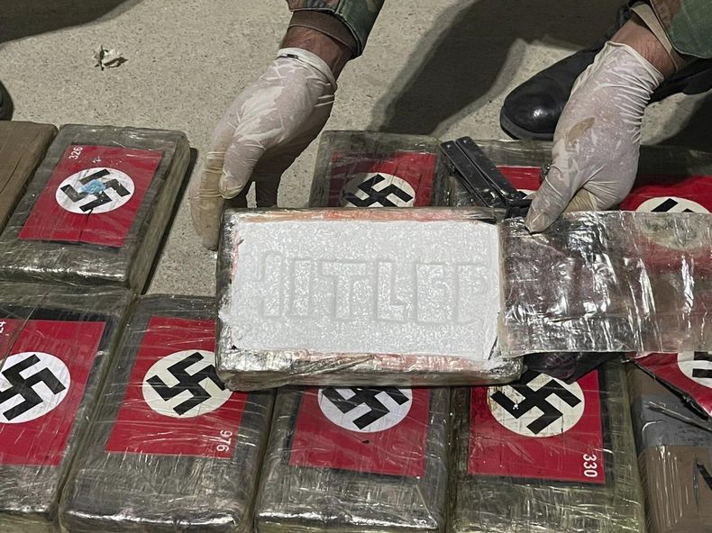 En esta imagen difundida por la Policía Antidrogas de Perú, un agente muestra paquetes de cocaína marcados con esvásticas nazis y el nombre Hitler, el jueves 25 de mayo de 2023, en el puerto de Paita, en la región de Piura, Perú. (Policía Antidrogas de Perú vía AP)