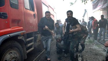 americateve | En esta imagen proporcionada por la agencia oficial de noticias siria SANA, soldados gubernamentales, derecha, y un civil, izquierda, trasladan hacia una ambulancia a un hombre herido por la explosi&oacute;n de un carro-bomba en una calle comercial en Hom