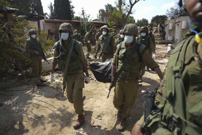 Soldados israelíes cargan el cuerpo de una persona que murió en un ataque de Hamas, el martes 10 de octubre de 2023, en el kibbutz Kfar Aza. Combatientes de Hamas incursionaron el sábado en el kibbutz, donde mataron y secuestraron a varios israelíes. (AP Foto/Erik Marmor)