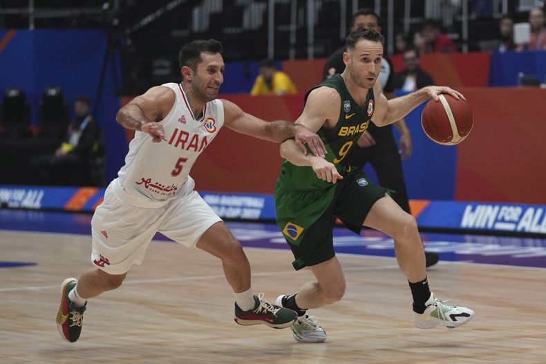 El brasileño Marcelo Huertas maneja el balón superando al base iraní Sajjad Mashayekhi en el encuentro del Grupo G de la Copa Mundial de baloncesto en Jakarta, Indonesia el sábado 26 de agosto del 2023. (AP Foto/Tatan Syuflana)