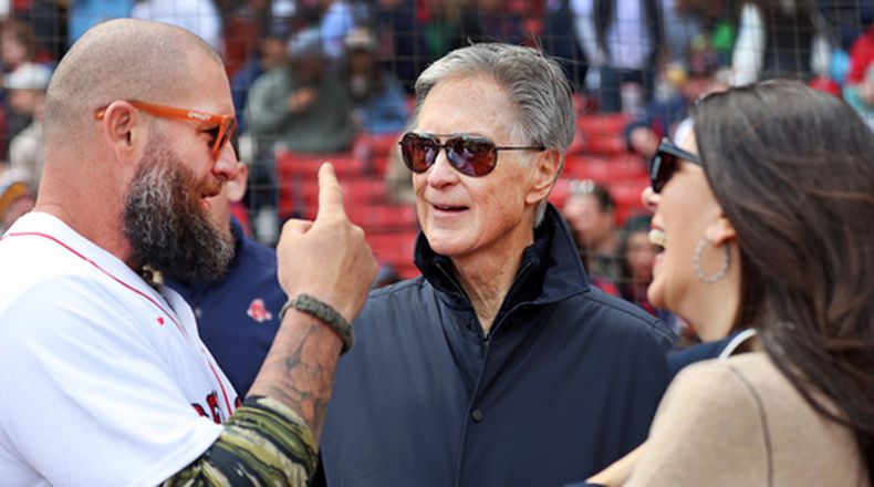 ARCHIVO - Desde la izquierda, Jonny Gomes, ex jugador de Medias Rojas, John Henry y su esposa, Linda Pizzuti Henry, propietarios de los Medias Rojas, hablan en el campo previo a un partido de béisbol de Grandes Ligas de los Medias Rojas contra los Tigres de Detroit, el 20 de abril de 2026, en Boston. (AP Foto/Jim Davis, Archivo)