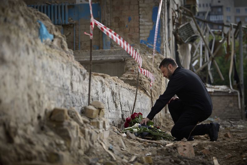 En esta fotografía proporcionada por la oficina de prensa de la presidencia ucraniana, el presidente de Ucrania, Volodymyr Zelenskyy, deja unas flores en el sitio donde se registró un ataque mortal con misiles ruso en un edificio residencial, en Kiev. (Oficina de prensa de la presidencia ucraniana vía AP)