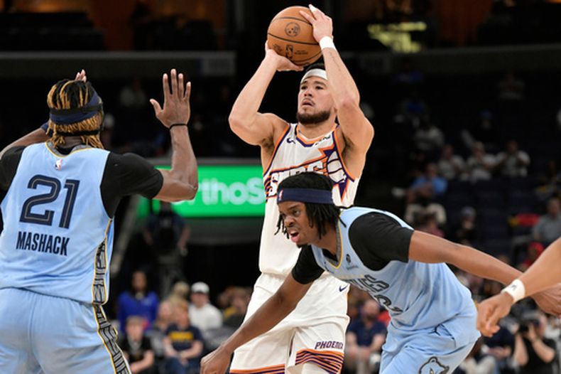 Devin Booker, de los Suns de Phoenix, dispara a la canasta sobre Jahmai Mashack (21) y Adama Bal, abajo de la derecha, de los Grizzlies de Memphis, en la segunda mitad del juego de baloncesto de la NBA, el lunes 30 de marzo de 2026, en Memphis, Tennessee. (AP Foto/Brandon Dill)