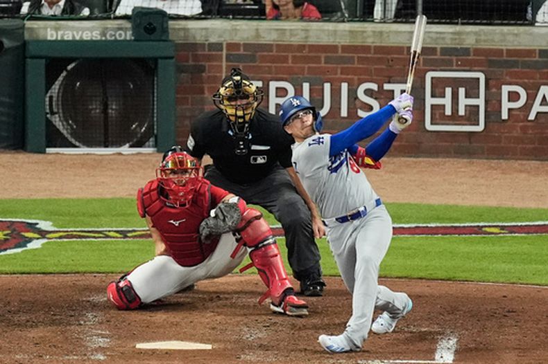 El infielder de los Dodgers de Los Ángeles, Enrique Hernández, completa su swing tras conectar un cuadrangular de dos carreras mientras el receptor de los Bravos de Atlanta, Drake Baldwin (30), y el ampáyer James Hoye observan durante la cuarta entrada del tercer juego de la serie divisional de la Liga Nacional de béisbol, el martes 6 de octubre de 2026, en Atlanta. (Foto AP/Mike Stewart)