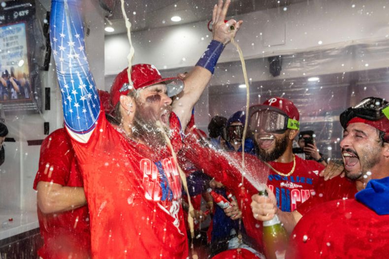 Bryce Harper (izquierda) recibe un baño de champaña durante la celebración de los Filis de Filadelfia tras obtener el pase de comodín al vencer a los Rays de Tampa Bay, el domingo 27 de septiembre de 2026, en Filadelfia. (AP Foto/Laurence Kesterson)