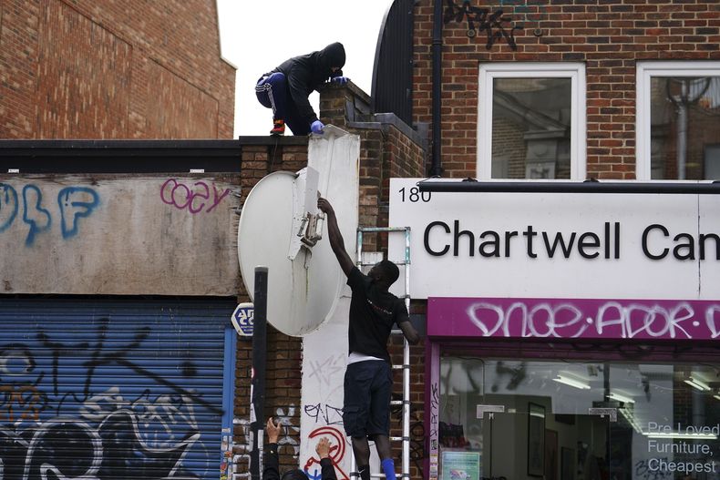 Personas retiran una nueva obra de arte de Banksy, que representa un lobo aullando pintado en una antena parabólica que se colocó en el techo de una tienda en Peckham, al sur de Londres, el jueves 8 de agosto de 2024. (Jordan Pettitt/PA vía AP)