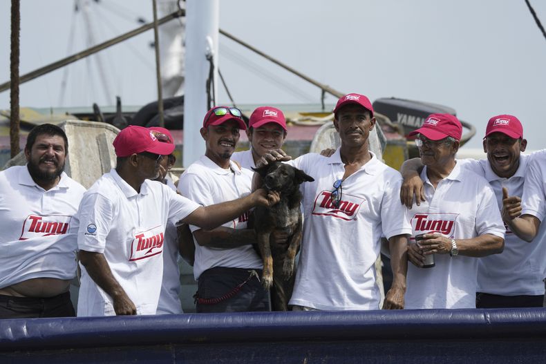 La tripulación del atunero mexicano María Delia posa para las fotos con Bella, la perra del australiano Timothy Lyndsay Shaddock, ambos rescatados de un catamarán dañado en el Océano Pacífico, a su llegada al puerto de Manzanillo, México, el martes 18 de julio de 2023. (AP Foto/Fernando Llano)
