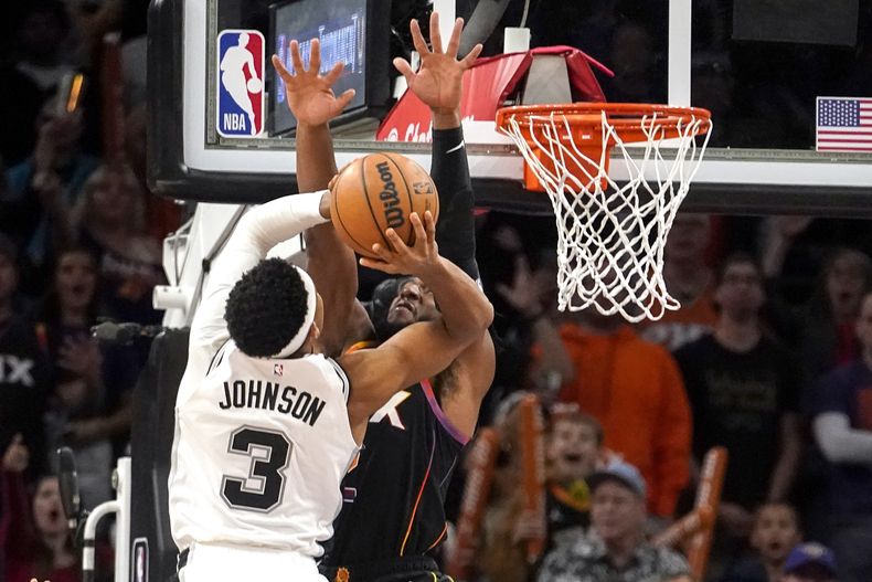 Keldon Johnson, de los Spurs de San Antonio, encesta frente a Josh Okogie, de los Suns de Phoenix, en el duelo del martes 31 de octubre de 2023 (AP foto/Darryl Webb)