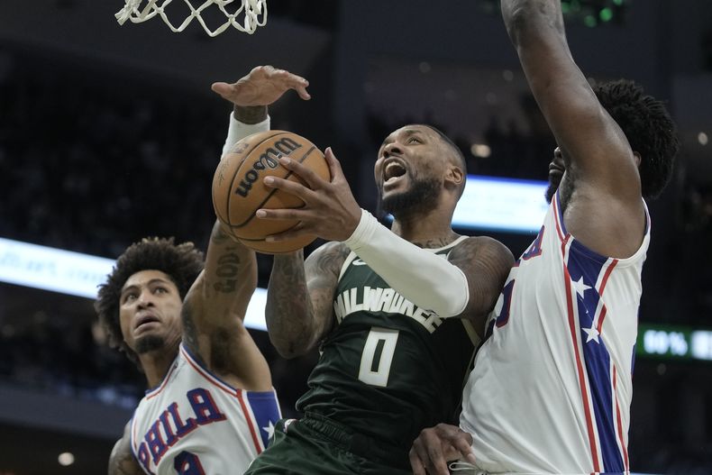 Damian Lillard, de los Bucks de Milwaukee, dispara entre Kelly Oubre Jr. y Joel Embiid, de los 76ers de Filadelfia, en el partido del jueves 26 de octubre de 2023 (AP Foto/Morry Gash)