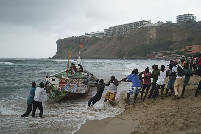 Un grupo de personas ayuda para sacar del mar un bote que, de acuerdo con testigos, naufragó en las costas de Dakar, Senegal, el lunes 24 de julio de 2023. (AP Foto/Leo Correa)