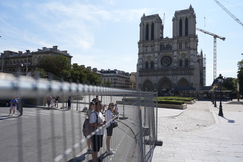 Personas intentan ver la catedral de Notre Dame desde el otro lado de la barrera después de que fuera instalado el perímetro de seguridad en las orillas del Sena antes de los Juegos Olímpicos el jueves 18 de julio del 2024. (AP Foto/David Goldman)