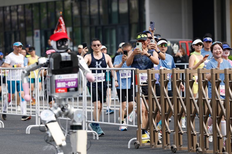 Corredores toman fotos de un robot humanoide en la II Media Maratón y Media Maratón de Robots Humaoides Beijing E-Town en Beijing, el domingo 19 de abril de 2026. (Haruna Furuhashi/Pool Foto via AP)