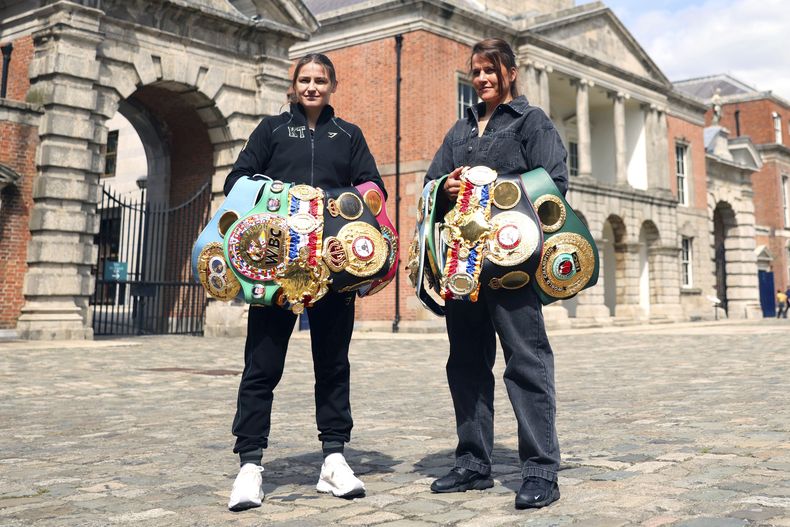 Katie Taylor (izquierda), monarca indiscutible de las ligeras y Chantelle Cameron, campeona indiscutible de las superligeras, posan frente al Castillo de Dublín, el jueves 18 de mayo de 2023 (AP Foto/Peter Morrison)