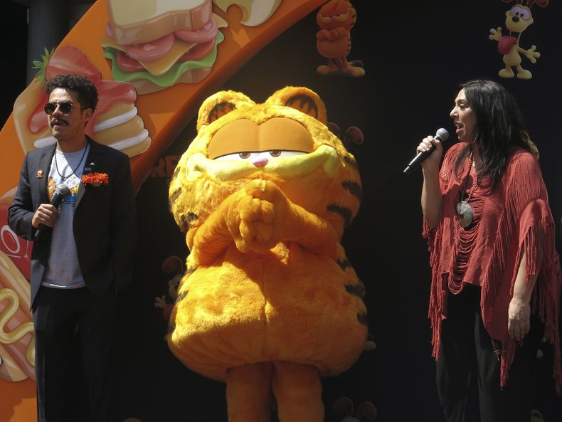 Un artista disfrazado como el personaje Garfield, centro, con los actores de doblaje Guillermo Memo Villegas, izquierda y Regina Orozco, derecha, en la alfombra naranja de la versión en español para Latinoamérica de The Garfield Movie en la Ciudad de México el domingo 28 de abril de 2024. (Foto AP/Berenice Bautista)